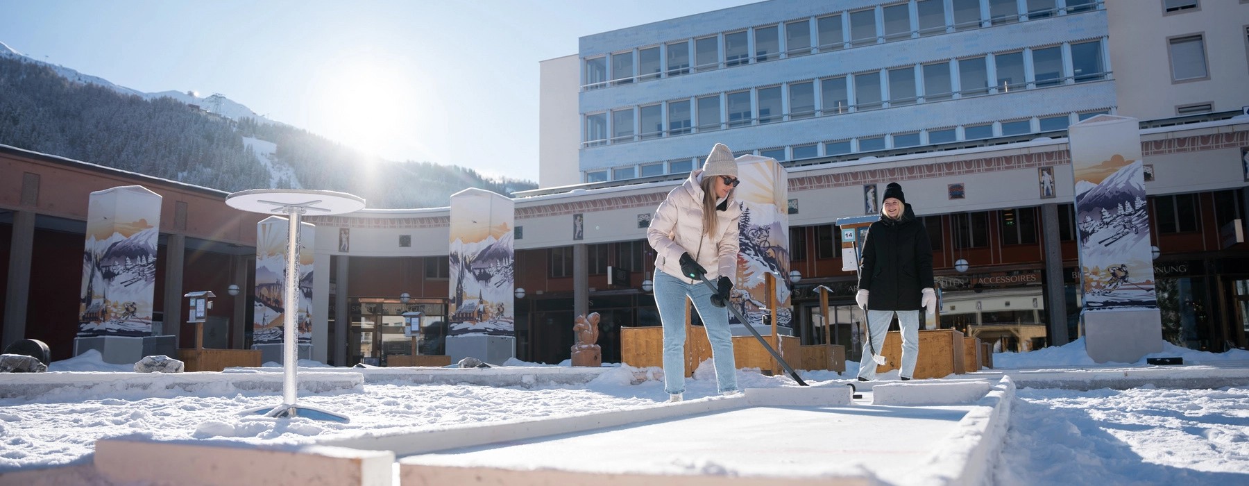 À Arkadenplatz, Davos, un parcours de 18 trous attend les amateurs de mini-golf devant un paysage de montagnes enneigées.